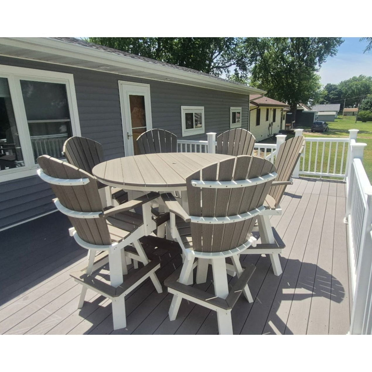 Outdoor patio with a round table and chairs on a deck, featuring a house and garden in the background.